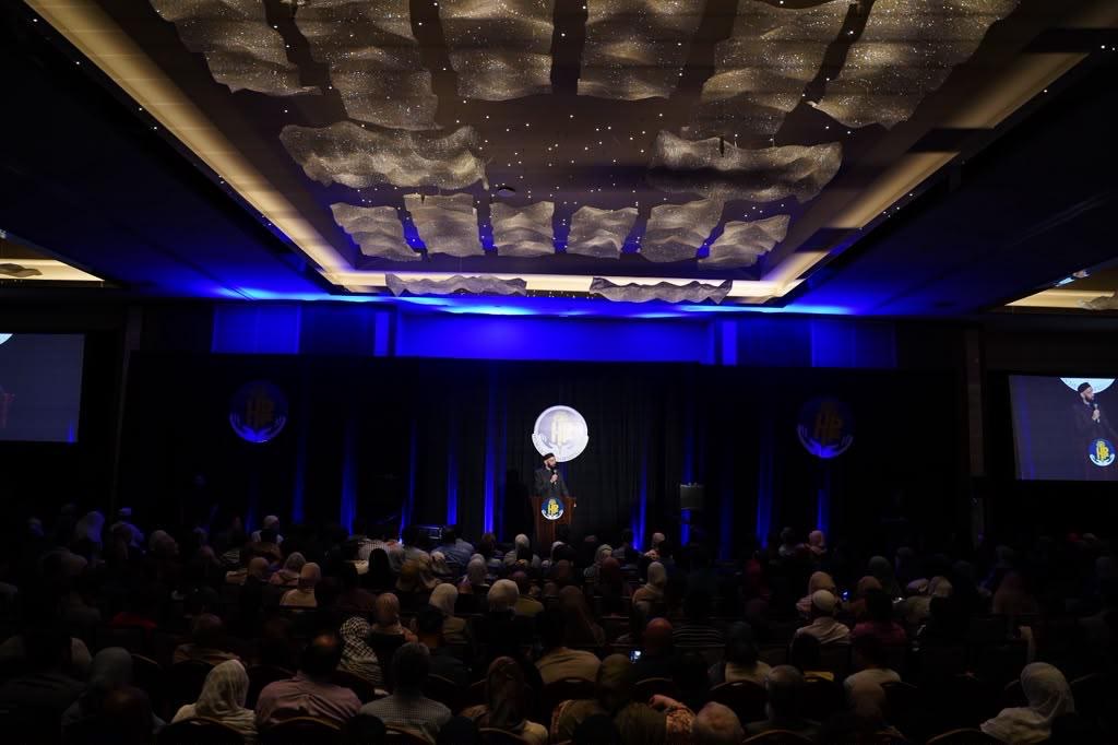 Wide view of a packed conference room with projection screens and blue lighting